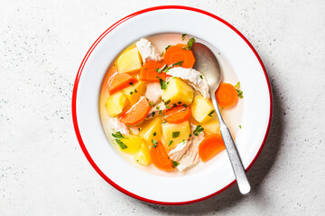 Traditional chicken soup with vegetables in white plate, gray background. Home cooking concept.