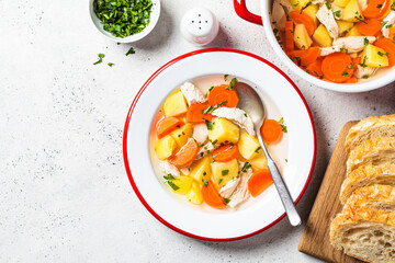 Traditional chicken soup with vegetables in white plate, gray background. Home cooking concept.