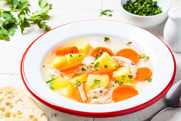 Traditional chicken soup with vegetables in white plate, gray background. Home cooking concept.