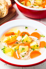 Traditional chicken soup with vegetables in white plate, gray background. Home cooking concept.