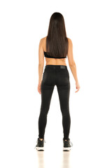 Rear view of a young woman in black jeans and short top posing on a white background