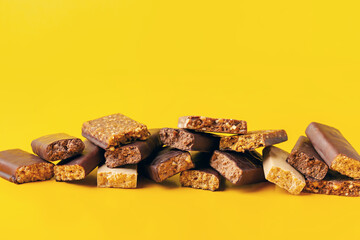 Whey protein powder in measuring scoop and different energy protein bar on yellow background.