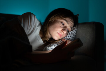 Unhappy woman lying in bed with smartphone, following ex-boyfriend on social media, sad female...