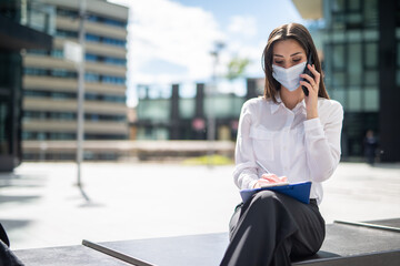 Fototapeta premium Masked woman talking on the phone while writing notes, covid and coronavirus concept