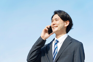 ビジネスマン　スマホ　電話する　青空背景