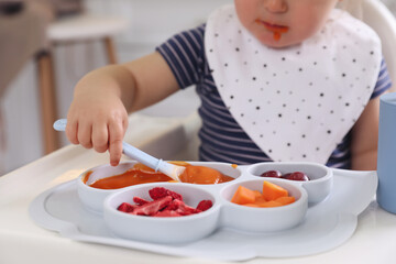 Little baby eating food in high chair at kitchen, closeup