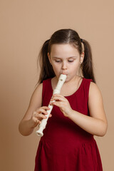 Girl in red dress play melody on flute with concentration, blowing air into duct, beige background....