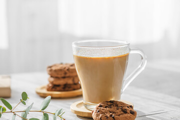 a transparent cup of coffee with milk with chocolate cookies at morning shadows and sun rays on gray background