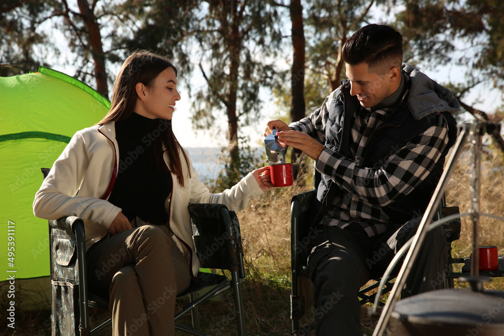 Poster couple resting in camping chairs and enjoying hot drink outdoors