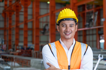 Selective focus at Asian men mechanical engineer, wearing safety equipment. While doing audit for quality and safety control inside of factory area. With blurred background of heavy machine.