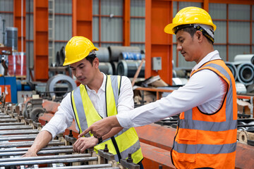 Selective focus at Asian men mechanical engineer, wearing safety equipment. While doing machine maintenance and safety control inside of factory area. With blurred background of heavy machine.