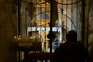 A silhouette of a person praying in a church in the shade against the background of a portrait of St. Peter