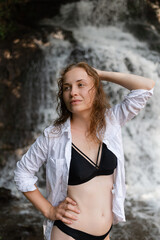 A portrait of a red-haired woman in a bathing suit in a waterfall background