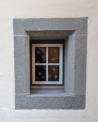 A very small, typically old window with stone details around it, deep into the facade and with window bars