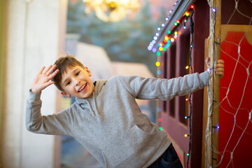 A happy little boy waves his hand from a toy wagon decorated with garlands.