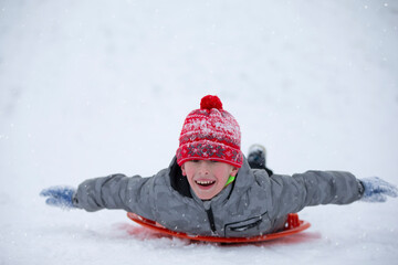 Fototapeta na wymiar Cute young boy smiling while he is sledding