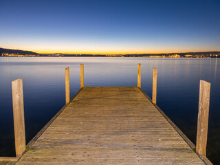 View onto horizon after the sunset on winter day in december with wooden pier in the foreground and city with light at the horizon