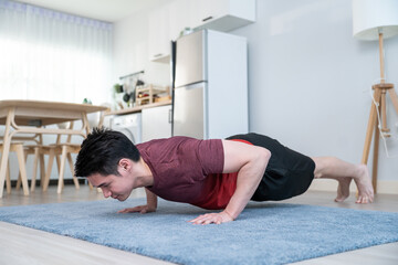 Fototapeta na wymiar Asian handsome active young man doing sit up on floor in living room. 
