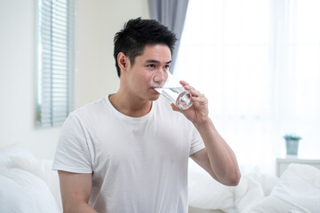 Portrait of Asian attractive male holding a glass of water in kitchen. 