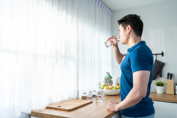 Asian attractive man holding a glass of clean water in kitchen at home