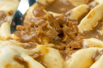 Close-up of scooping caramel ice cream with a dessert spoon. Macro photography of ice cream with caramel.