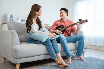 Asian young loving couple play guitar together in living room at home. - Powered by Adobe
