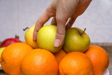 Close-up of a woman's hand taking a green apple from a plate of fruit orange and apples