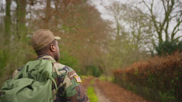 Rear view of soldier in camouflage uniform carrying kit bag walking home to see family on leave - shot in slow motion