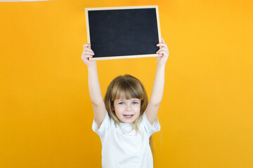 girl holding a board sheet. Cute little girl with chalk board. yellow background. copy space.