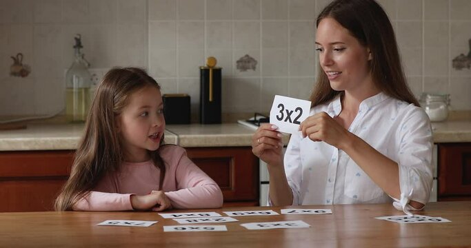 Young friendly loving mother or tutor showing flashcards to cute preschool girl, tests knowledge of multiplication basics at math lesson at home. Preparation for school, children development concept