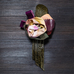 top view of handcrafted leather and silk brooch stylized as rose flower on dark wooden board