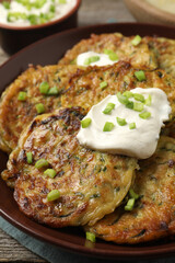 Delicious zucchini pancakes with sour cream and green onion on table, closeup