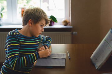 Hard-working school kid boy making homework during quarantine time from corona pandemic disease....