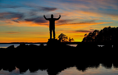 Silhouette of man standing strong infront of sunset and lake