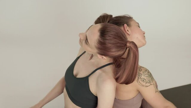 two women practice partner yoga, neck warm-up in a light studio