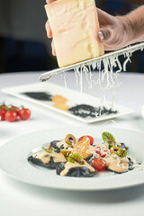 Chef decorates a dish of ravioli on a plate, rubbing Parmesan