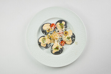 Black ravioli with red fish, sauce and tomatoes in a plate