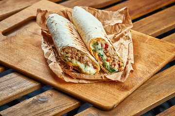 Large shawarma with meat and vegetables in kraft paper on a wooden background