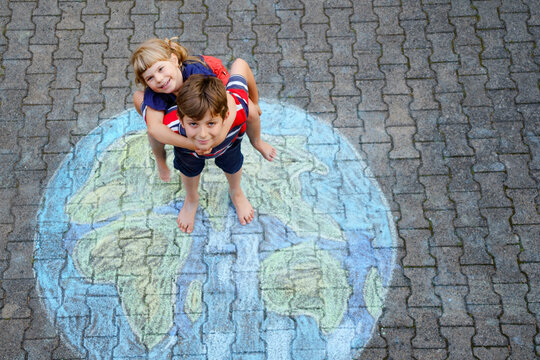 Little preschool girl and school kid boy with earth globe painting with colorful chalks on ground. Happy peace day concept. Creation of children for saving world, environment and ecology
