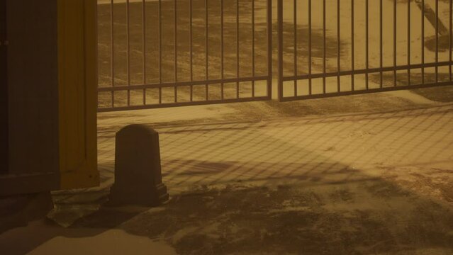 Snow drift over driveway, blowing wind drifting snow on asphalt, courtyard fence gate of residential building at night in winter. High quality 4k footage
