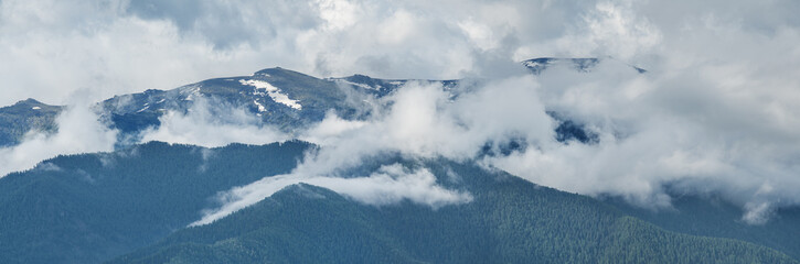 Snow covered mountain peaks in the clouds. Panoramic view.