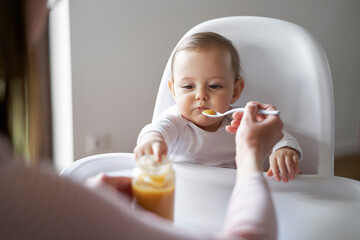 Mom feeding baby girl in high chair at home