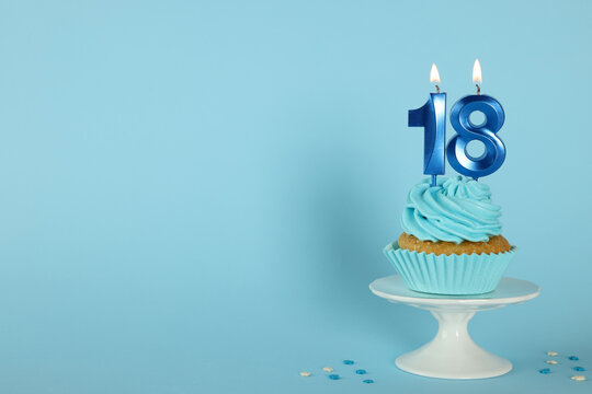 Delicious cupcake with number shaped candles on light blue background, space for text. Coming of age party - 18th birthday