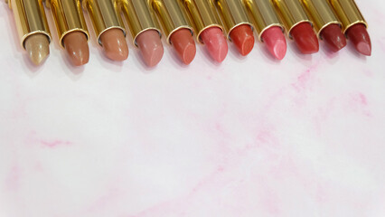 Lipsticks in different hues of red lined up side by side, on a pink marble background. With copy space on the bottom part.
