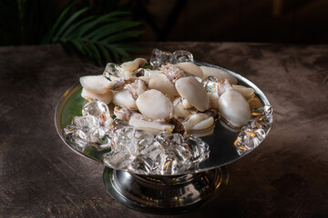 Fresh sea scallops among ice on a copper tray in a dark room