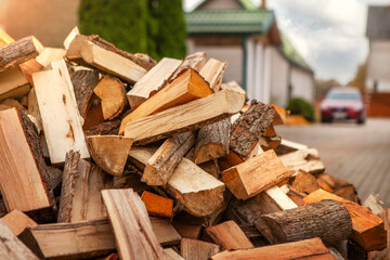 A pile of split firewood for heating the house, unloaded in the yard, against the backdrop of the house, natural heating sources.