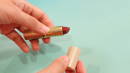 Hand holding a tube of red lipstick, with the other hand holding the lid.