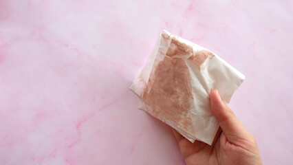 Hand holding a piece of tissue paper with stain from wiping off makeup powder.