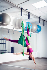 Profesora joven de yoga aéreo con telas verdes. Mujer chica blanca caucásica imparte una clase...