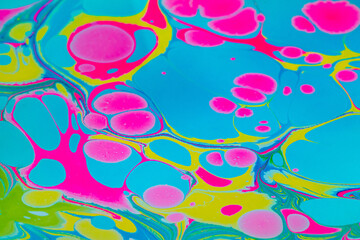 Fototapeta premium Colorful background with pink, blue and yellow marble spots in Turkish ebru technique. Unique artistic marble texture background, drawing with acrylic paints on the surface of the water. Close up.